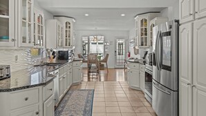 A spacious kitchen with white cabinetry, a large stainless steel refrigerator, and a dining area with a table and chairs. - Lakeview Escape. Hot Tub, Sauna, Screened Porch. Birding Paradise. Wineries! (Amherstburg)
