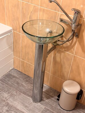 A bathroom with a glass sink, a toilet, and a trash bin. - Charming Birmingham Apartment With Mini Balcony and Wifi With a Free Parking (Birmingham)
