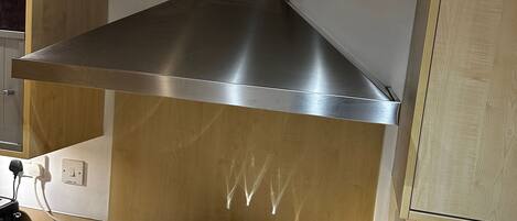 A kitchen with a stainless steel range hood, a stove with pots and a pan, and a coffee maker.