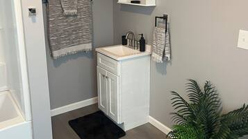 A bathroom with a white vanity, a towel rack, a sink, and a potted plant.