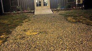 A building with a gravel driveway and a wooden deck leading to a set of double doors.