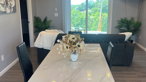 A modern dining area with a marble table, black chairs, and a vase of flowers. There is a ceiling fan and recessed lighting.