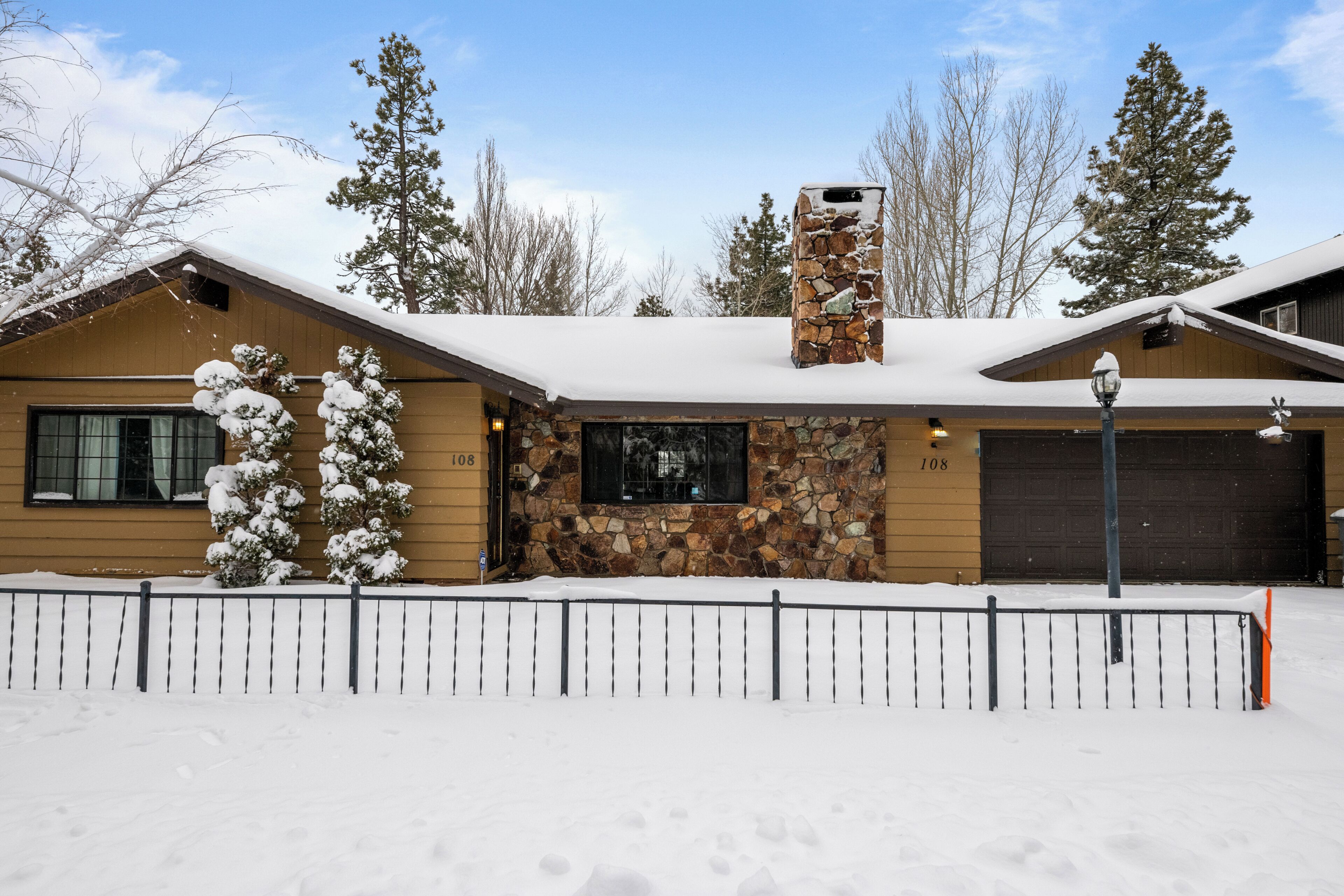 A two-story house with a stone chimney, a garage, and a snow-covered roof.