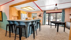 A kitchen with wooden cabinets, a bar area with stools, and a foosball table.