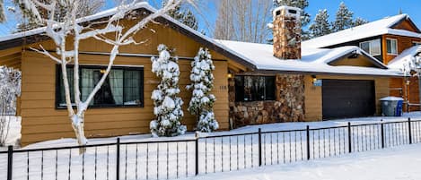 A two-story wooden house with a stone chimney, a garage, and a snow-covered landscape.