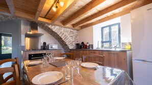 A dining area with a wooden table set for four, a stone wall, and a kitchen with modern appliances.