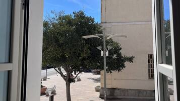 A window view of a building with a tree in the foreground, a clear sky, and a street with parked cars.