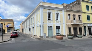 Une rue bordée d’un immeuble jaune doté d’un balcon, d’une voiture rouge garée sur le côté et d’un panneau de signalisation bleu indiquant un espace de stationnement.