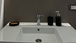 Une salle de bain avec un lavabo blanc, un miroir rond avec un éclairage intégré et un distributeur de savon noir.