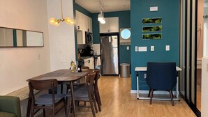 A modern kitchen with stainless steel appliances, a dining area with wooden furniture, and a teal accent wall with greenery. - Jr 1 BR w/ parking & a plunge in Design District (San Francisco)