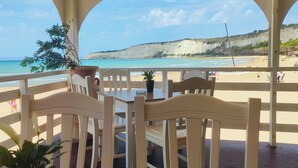 Une terrasse au bord de la plage, avec une table et des chaises, d’où l’on peut admirer une plage de sable et une falaise.