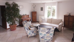 A living room with a sofa, armchairs, a coffee table, a potted plant, and a wooden cabinet.