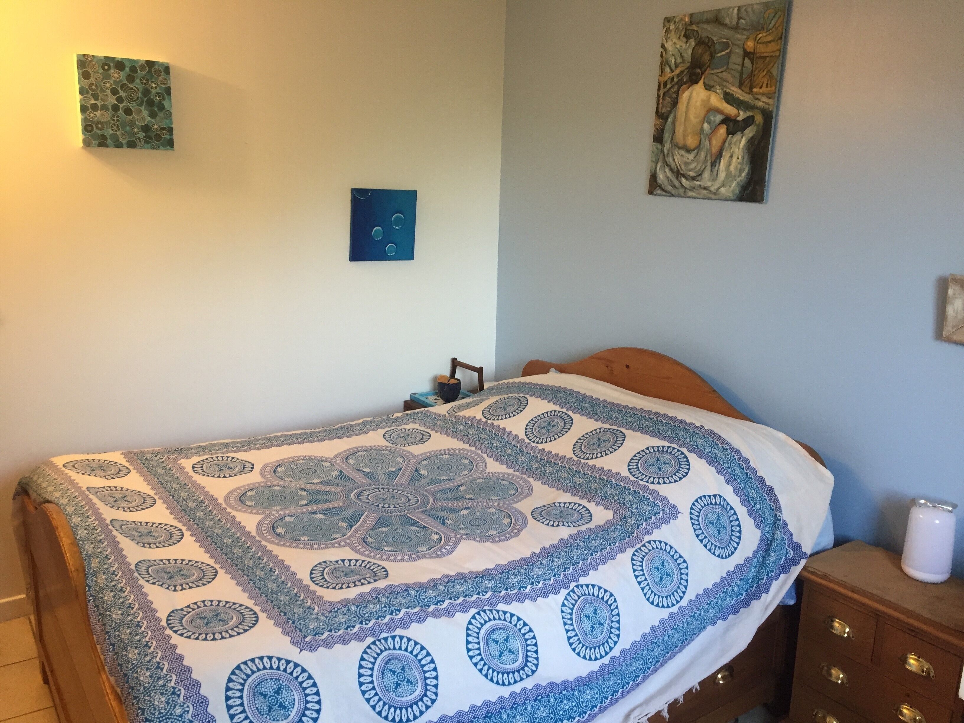 A bedroom with a bed, a nightstand, a dresser, and two wall art pieces.