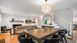 Un salon spacieux avec une table à manger en bois, des chaises en cuir noir, une cheminée, un escalier et un grand miroir.