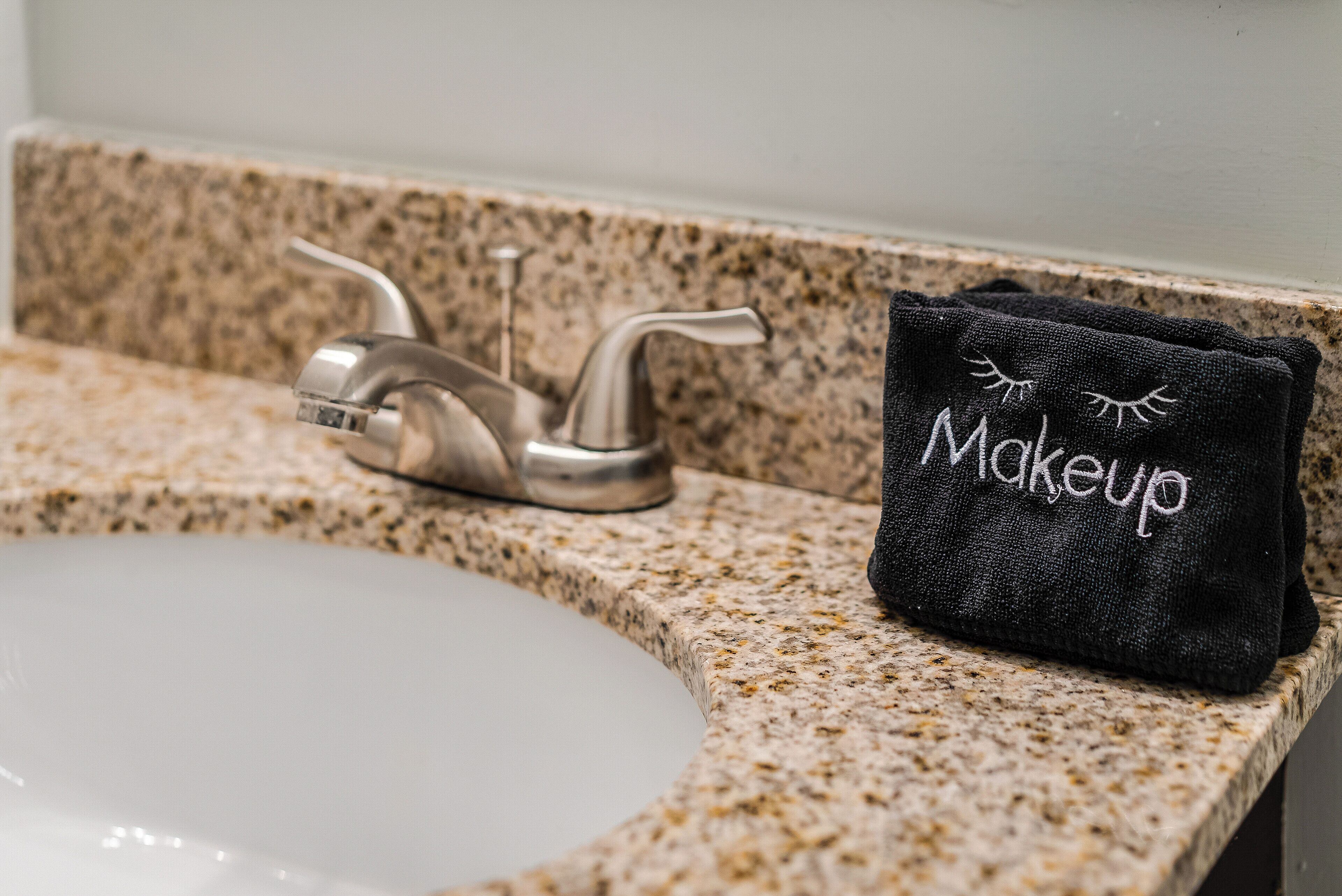 Un lavabo de salle de bain avec un plan de toilette en granit et une serviette sur laquelle est brodé le mot « Maquillage ».
