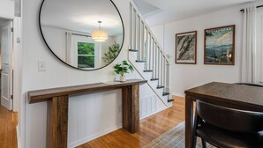 Un escalier avec des rampes blanches et une main courante en bois, un miroir rond accroché au mur et deux tableaux encadrés sur le mur.