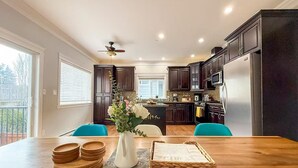 A modern kitchen with dark wood cabinets, a central island, and a dining area with a wooden table.