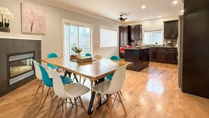 A modern kitchen with dark cabinets, a central island, and a dining area with a wooden table and blue chairs.
