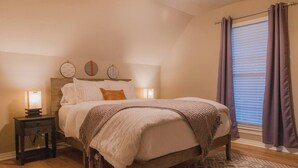A bedroom with a bed, bedside tables, a window with curtains, and a patterned rug. - Spacious Home in South Tulsa- Finale Home. Close to major highways and Riverside (Tulsa)