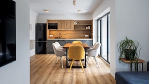 Una cocina moderna con armarios de madera, un refrigerador negro y un comedor con una mesa de madera y cuatro sillas.