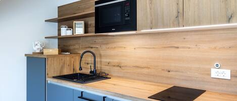 A modern kitchen with wooden cabinetry, a black microwave, and a sink with a black faucet.