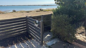 A wooden gate leading to a beach with a clear view of the sea and distant buildings.