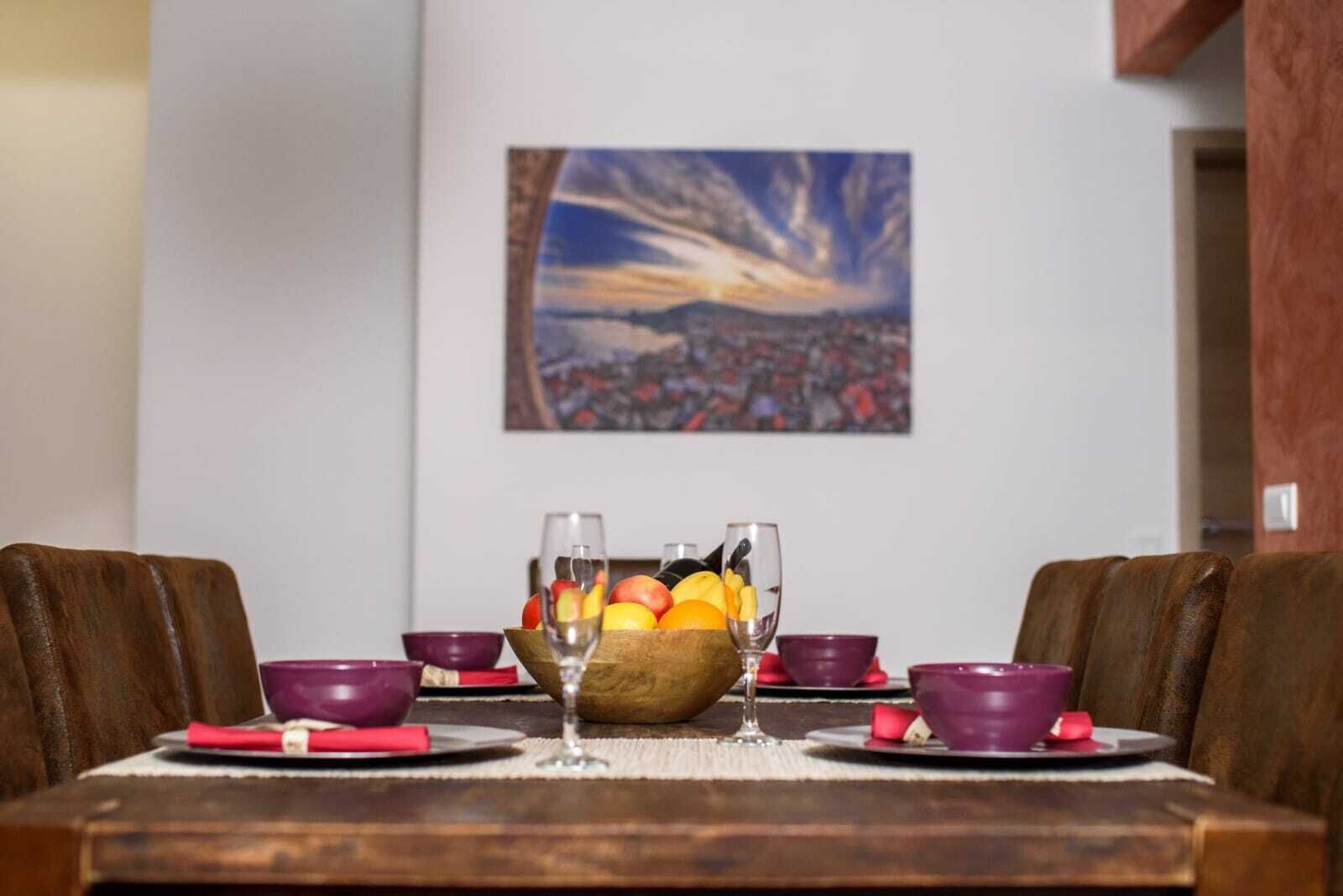 A dining table set with red and purple bowls, a fruit bowl, and wine glasses.