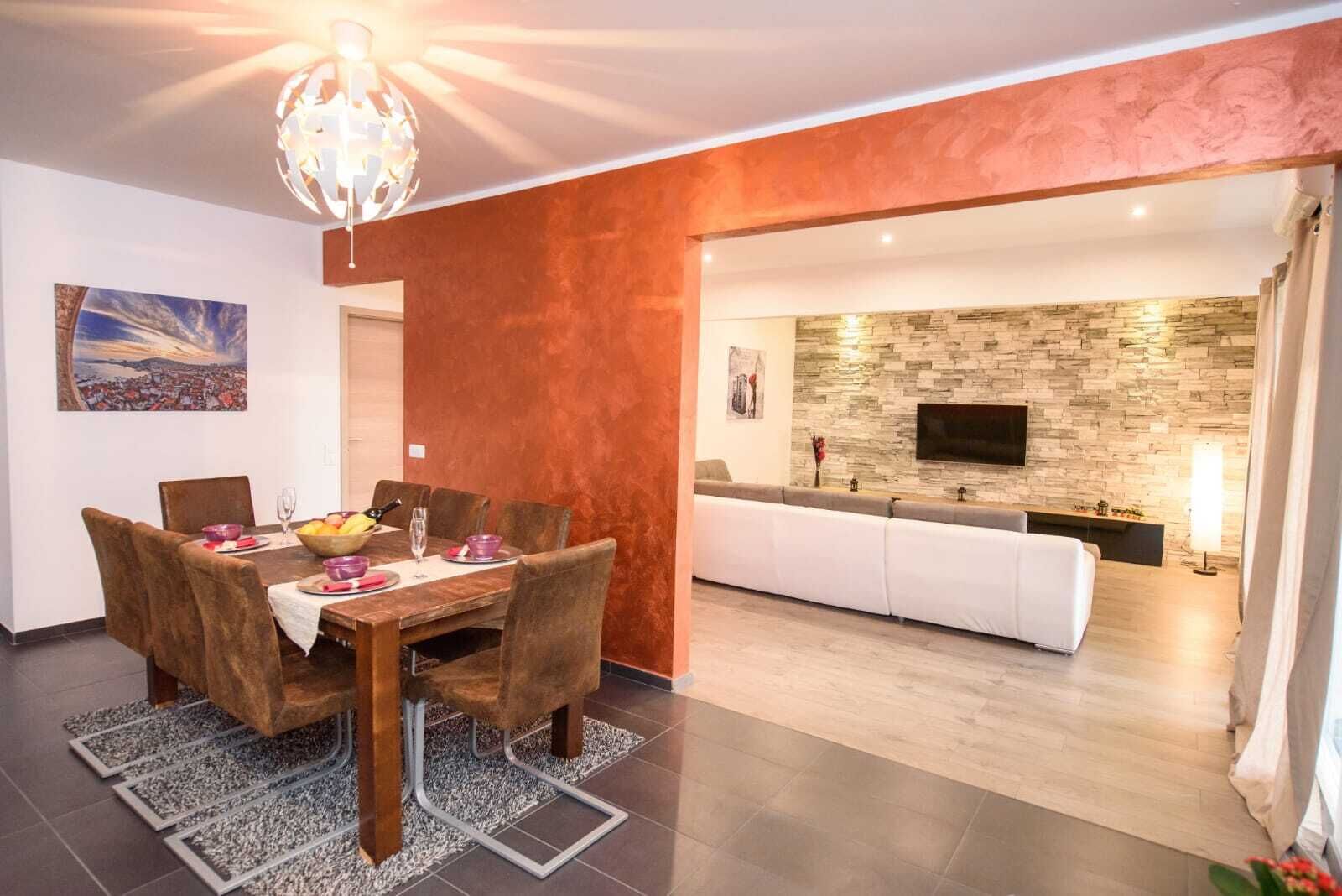 Zona pranzo moderna con tavolo e sedie in legno, una ciotola di frutta e un lampadario.