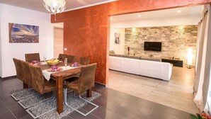 A modern dining area with a wooden table and chairs, a fruit bowl, and a chandelier. - Vacation home near Split with private pool & garden (Kaštel Lukšić)