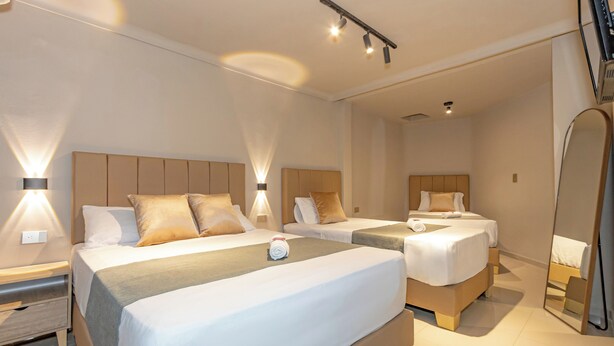 Habitación de hotel con dos camas, una mesita de noche, un espejo y una lámpara en el techo.