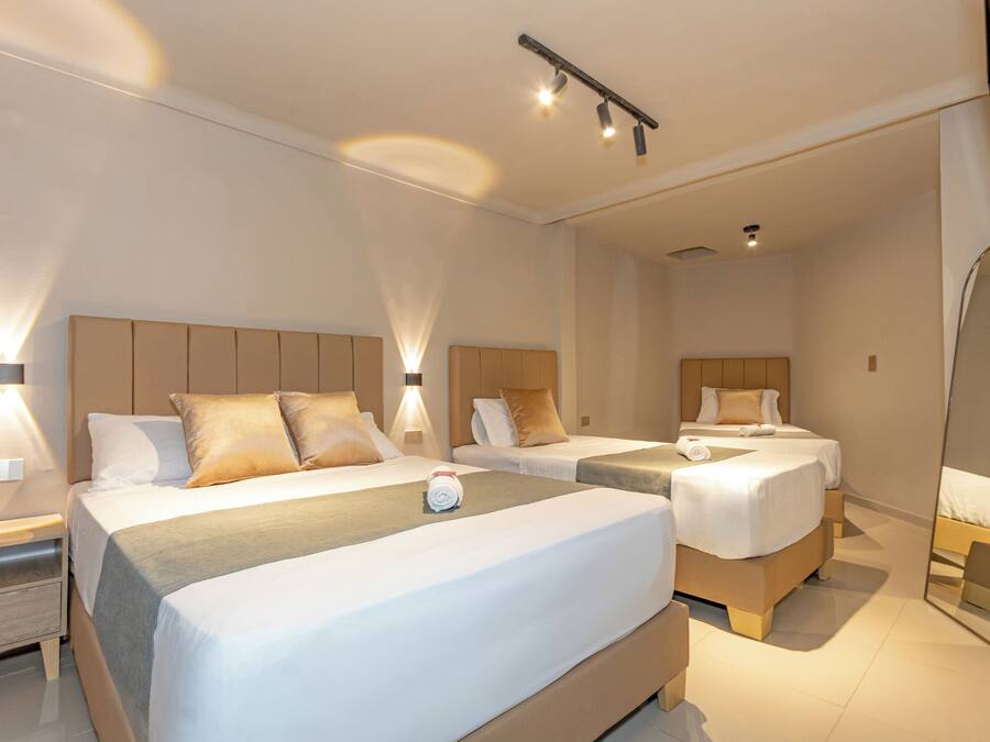 Habitación de hotel con dos camas, una mesita de noche, un espejo y una lámpara en el techo.