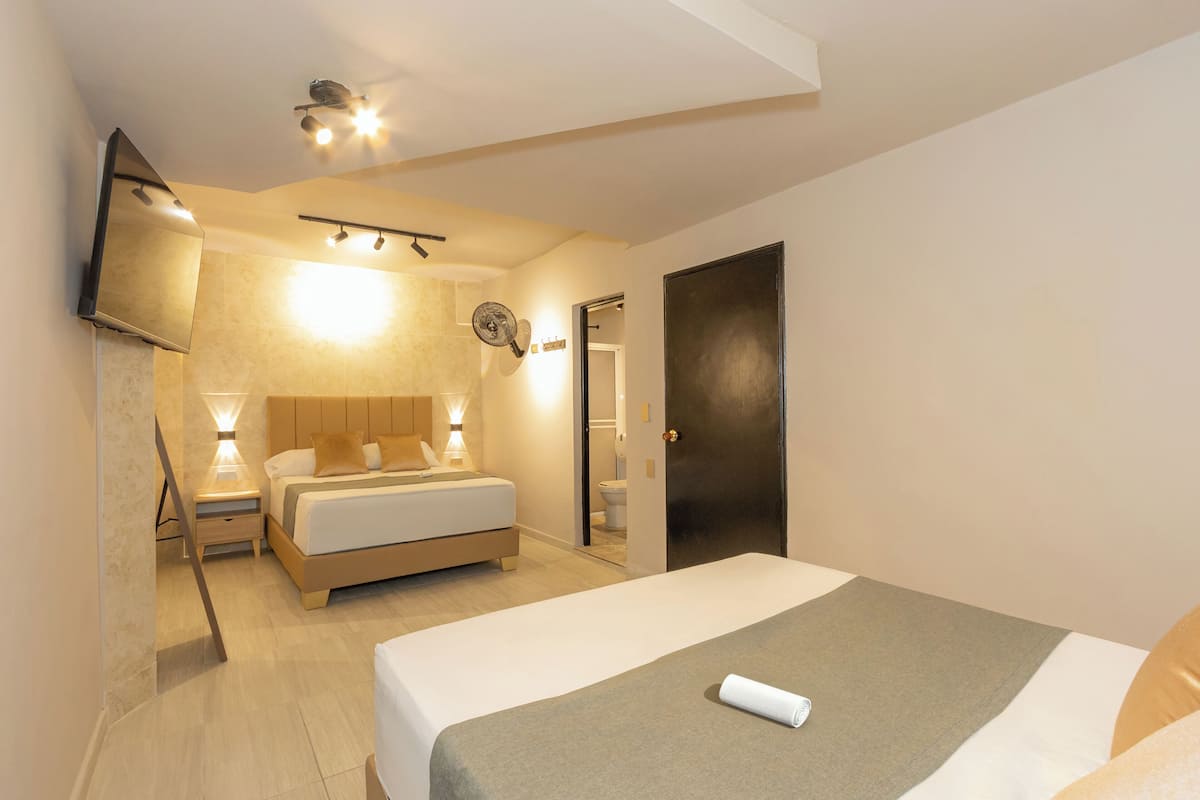 Ein modernes Hotelzimmer mit einem großen Bett, Nachttischen, einem flachbildfernseher an der Wand und einer Tür zum Badezimmer.