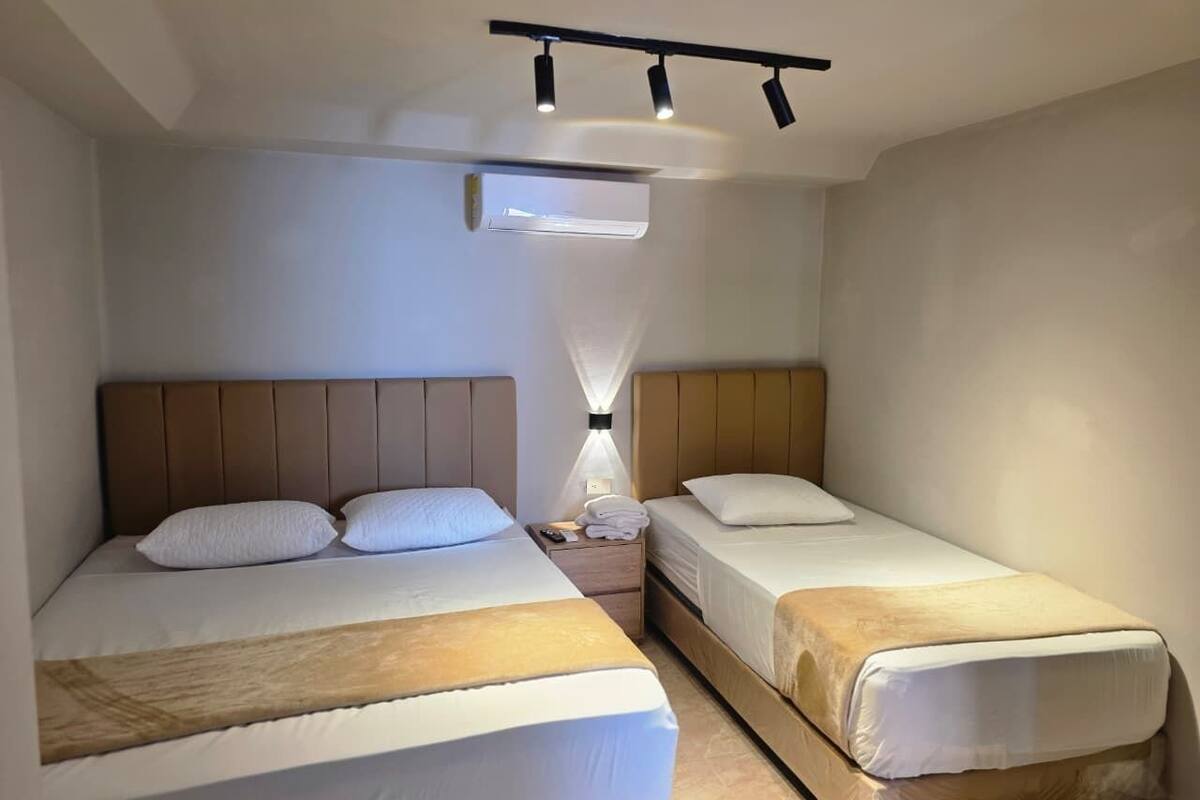 Ein Hotelzimmer mit zwei Betten, einem Nachttisch mit Lampe und einer Decken-Klimaanlage.