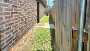 Un estrecho callejón de ladrillo con una valla de madera a un lado y una zona verde al otro.