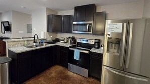 Una cocina moderna con armarios oscuros, electrodomésticos de acero inoxidable, encimera de granito y alfombra marrón.