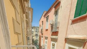 Un estrecho callejón entre edificios con balcones, una barandilla de metal y un cielo azul despejado.
