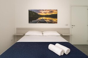 A hotel room with a bed, two pillows, a blue polka dot bedspread, and a painting of a sunset over a river.