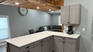 A modern kitchen with grey cabinets, a white countertop, and a wooden ceiling.