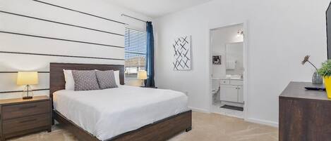 Quarto com cama, mesas de cabeceira, um espelho e uma porta de entrada para o banheiro.