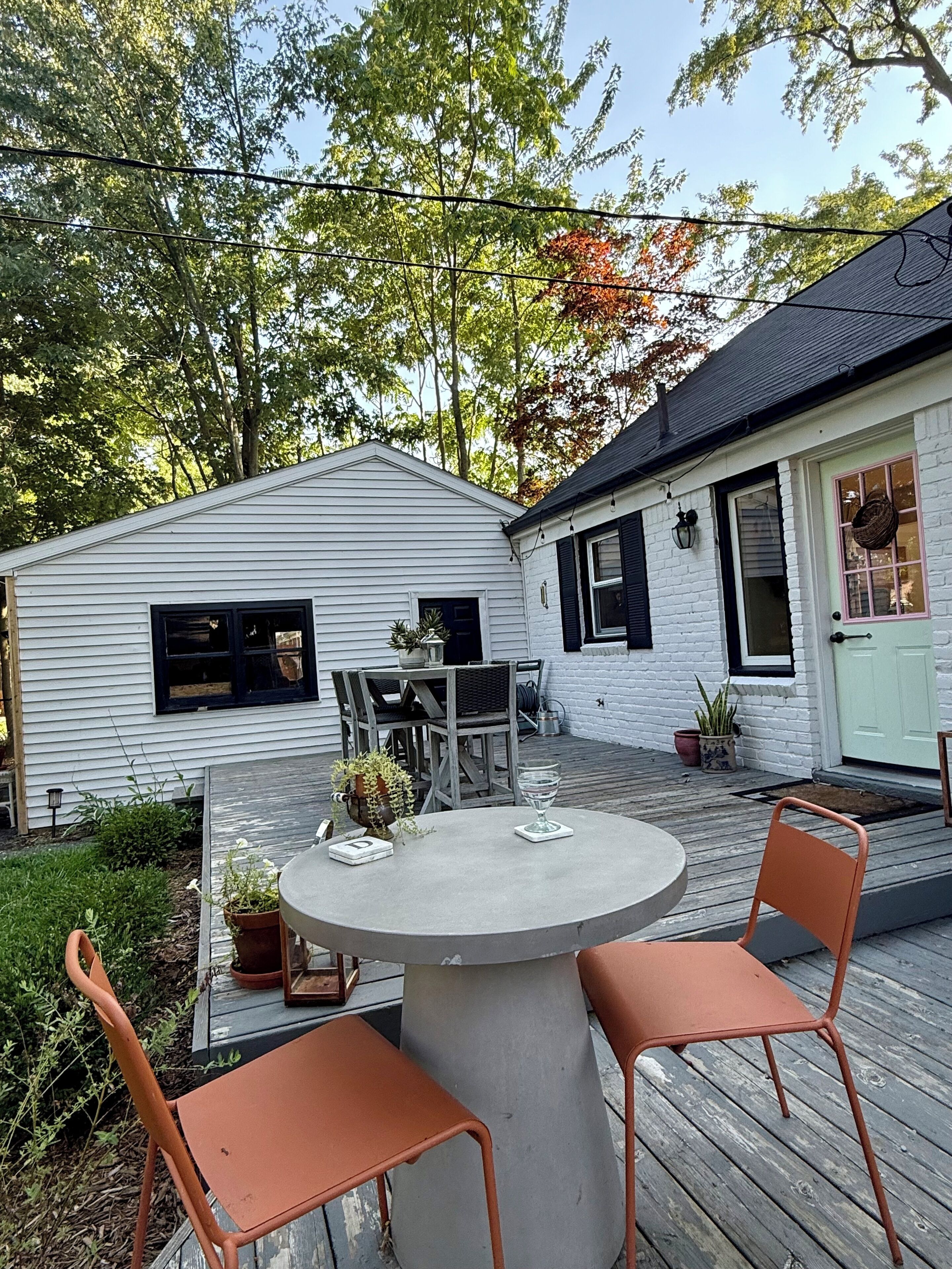 A patio with a round table and two chairs, surrounded by potted plants and a small garden.