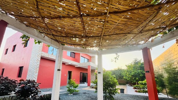A covered outdoor area with a red building in the background. - Authentic stay at Villa Noflaye du Lac Rose! (Deni Biram Ndao)