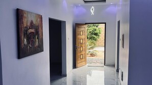 A hallway with a marble floor, a wooden door, and a modern light fixture. - Authentic stay at Villa Noflaye du Lac Rose! (Deni Biram Ndao)