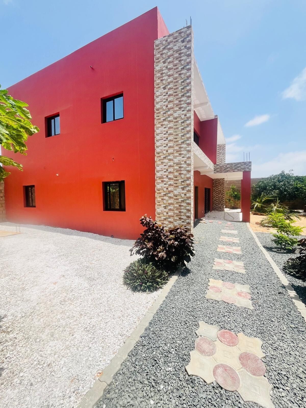 A modern building with a red facade, a central column, and a gravel pathway with decorative tiles.