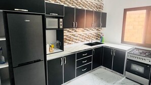 A modern kitchen with black cabinets, a stainless steel refrigerator, a microwave, and a gas stove. - Authentic stay at Villa Noflaye du Lac Rose! (Deni Biram Ndao)