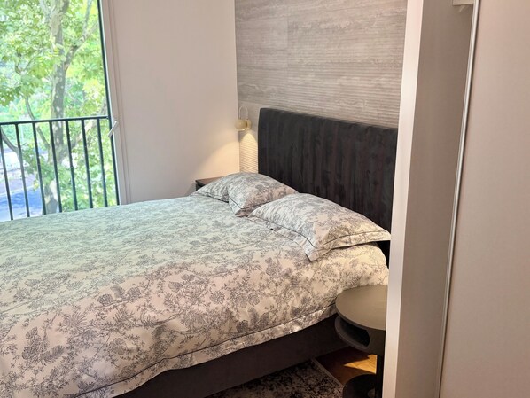 Un dormitorio con cama, mesita de noche, lámpara y vista a zonas verdes.