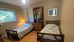 Une chambre à coucher avec deux lits en bois, un ventilateur de plafond, une fenêtre avec des rideaux, une commode et un tableau encadré au mur.