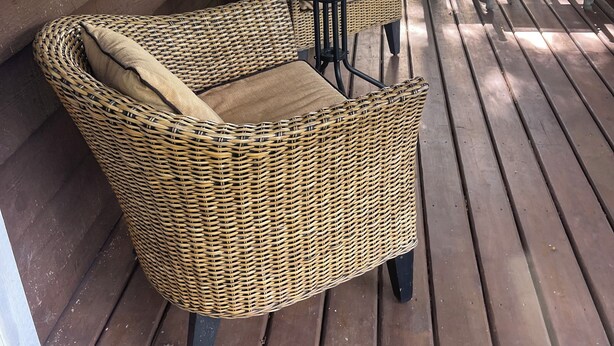 Un patio couvert aménagé avec des meubles en osier, comprenant deux chaises et une table, ainsi qu’un barbecue.