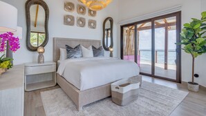 A bedroom with a large bed, multiple mirrors, a chandelier, and a view of the sea through large glass doors. - Magenta Caye Luxury Private Island Resort - All inclusive (Placencia)