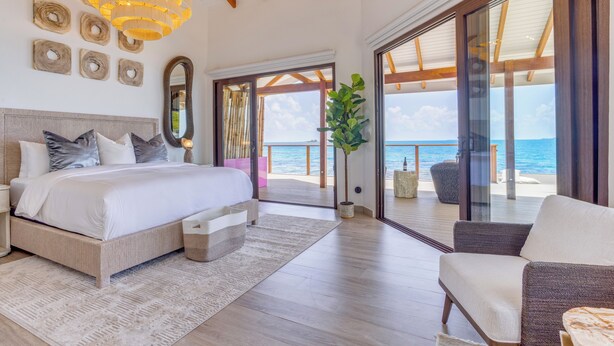 A bedroom with a large bed, a view of the sea, and a balcony with seating. - Magenta Caye Luxury Private Island Resort - All inclusive (Placencia)