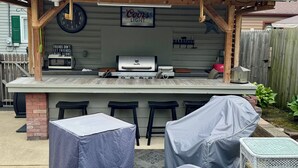 An outdoor bar area with a Coors Light sign, a clock, a barbecue grill, and covered seating.